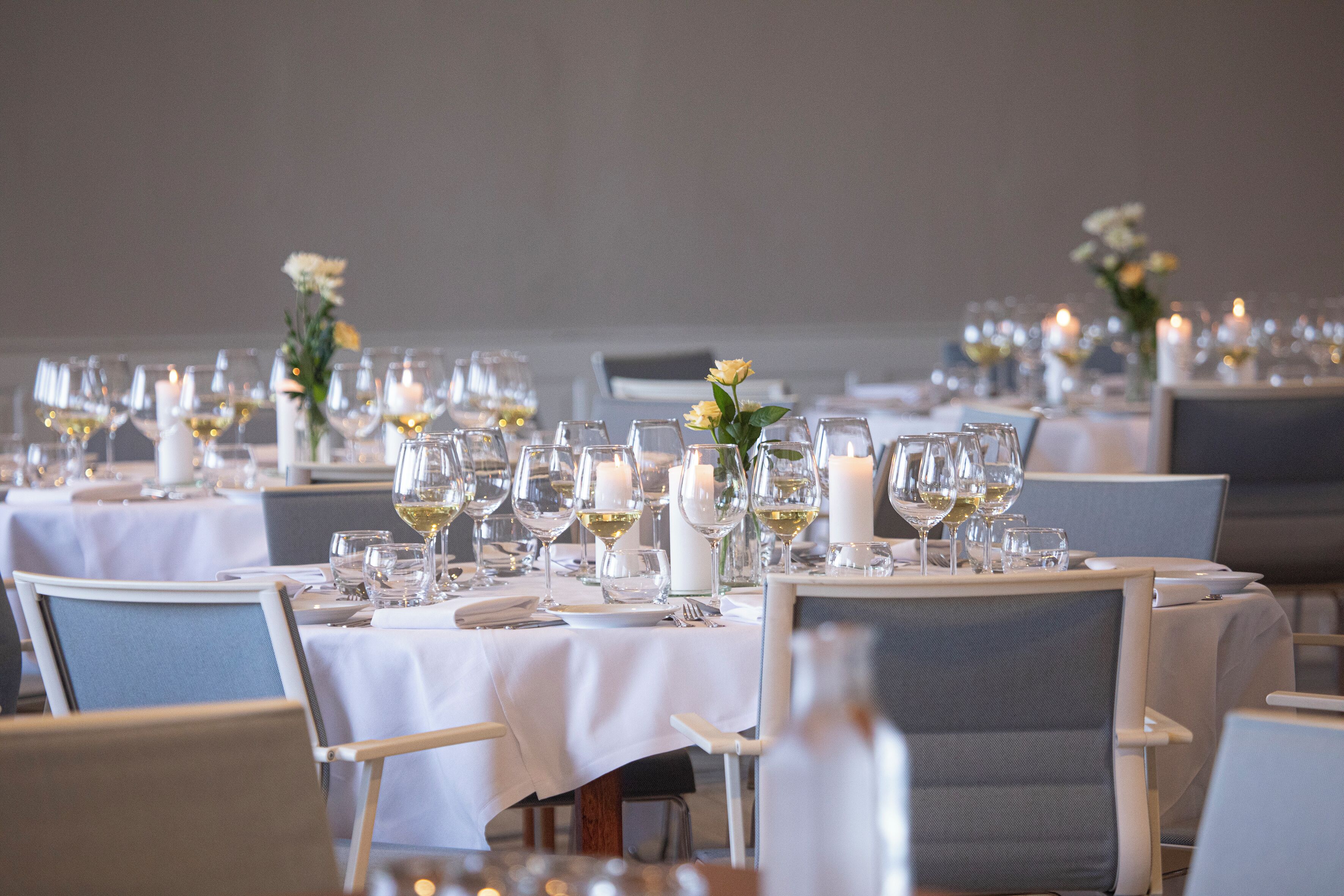 Ein Restaurant mit runden Tischen, gedeckt mit weißen Tischdecken, Kerzen und Weingläsern.