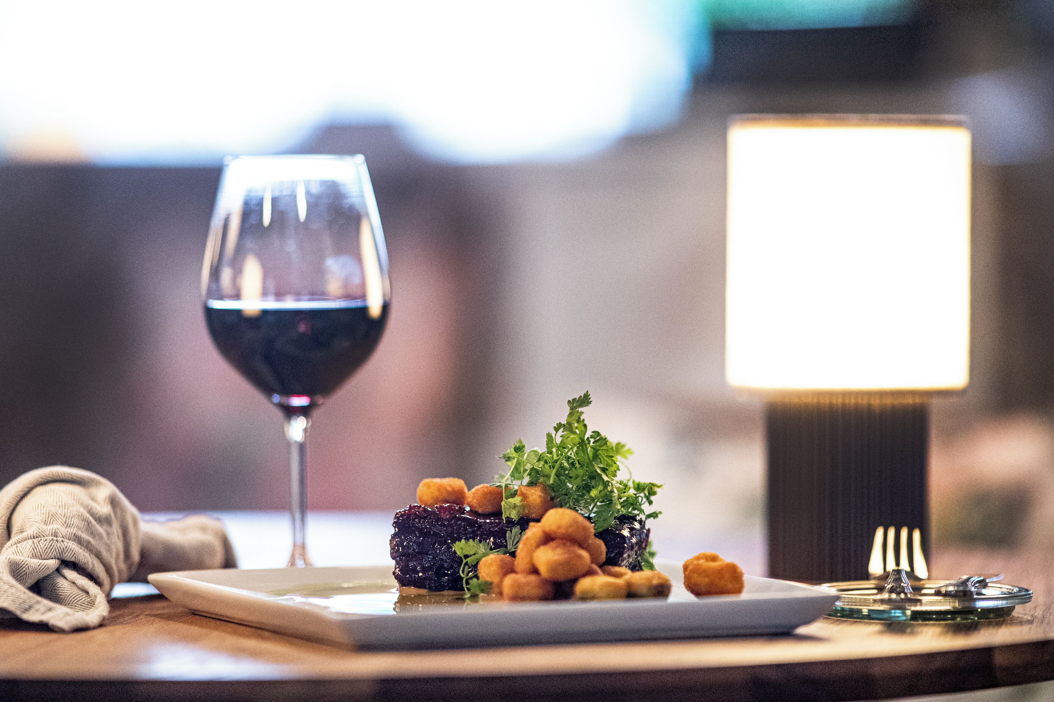 A dining table with a plate of food, a wine glass, and a lamp.
