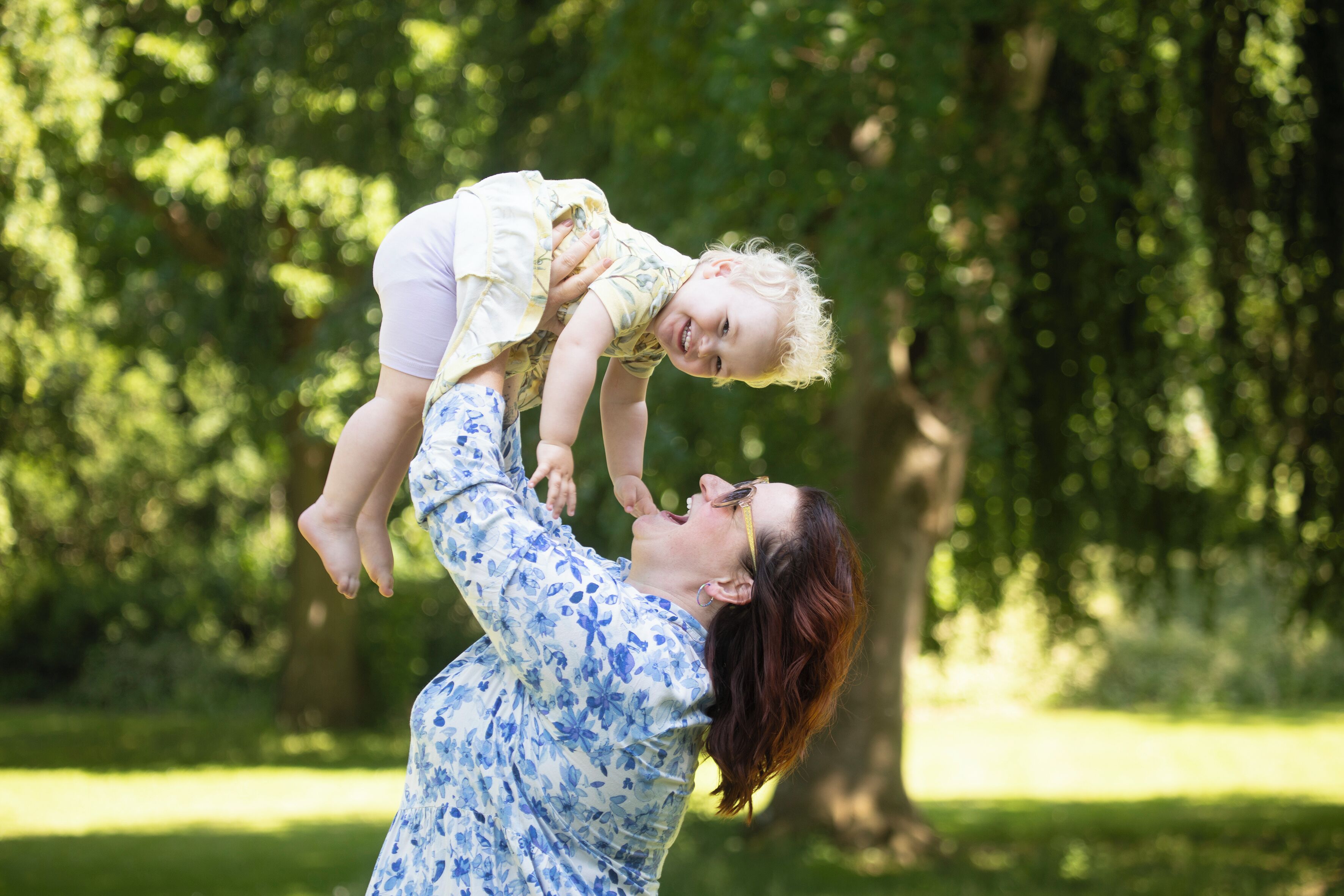 A person holding a child in a park with trees in the background.