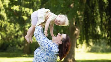 A person holding a child in a park with trees in the background.