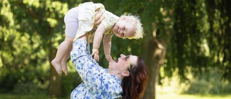 A person holding a child in a park with trees in the background.