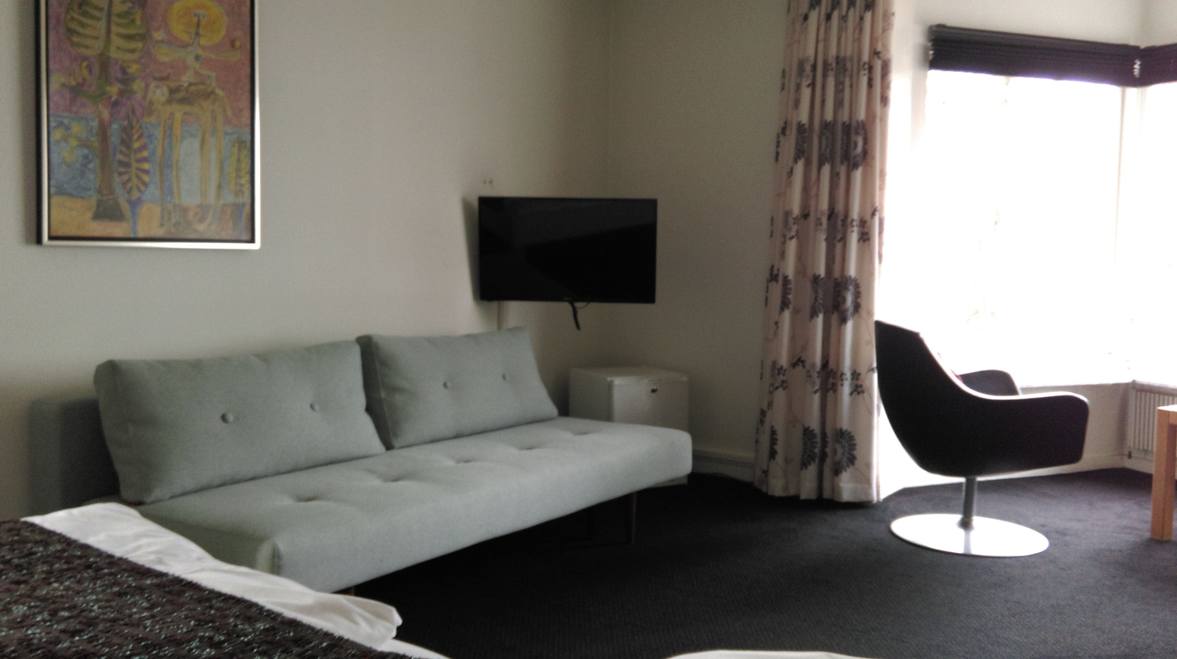 Una habitación de hotel con sofá, sillón, televisor y cama.