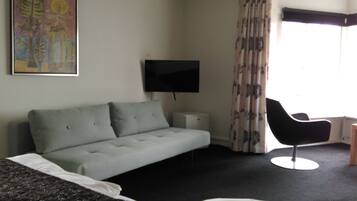 Una habitación de hotel con sofá, sillón, televisor y cama.
