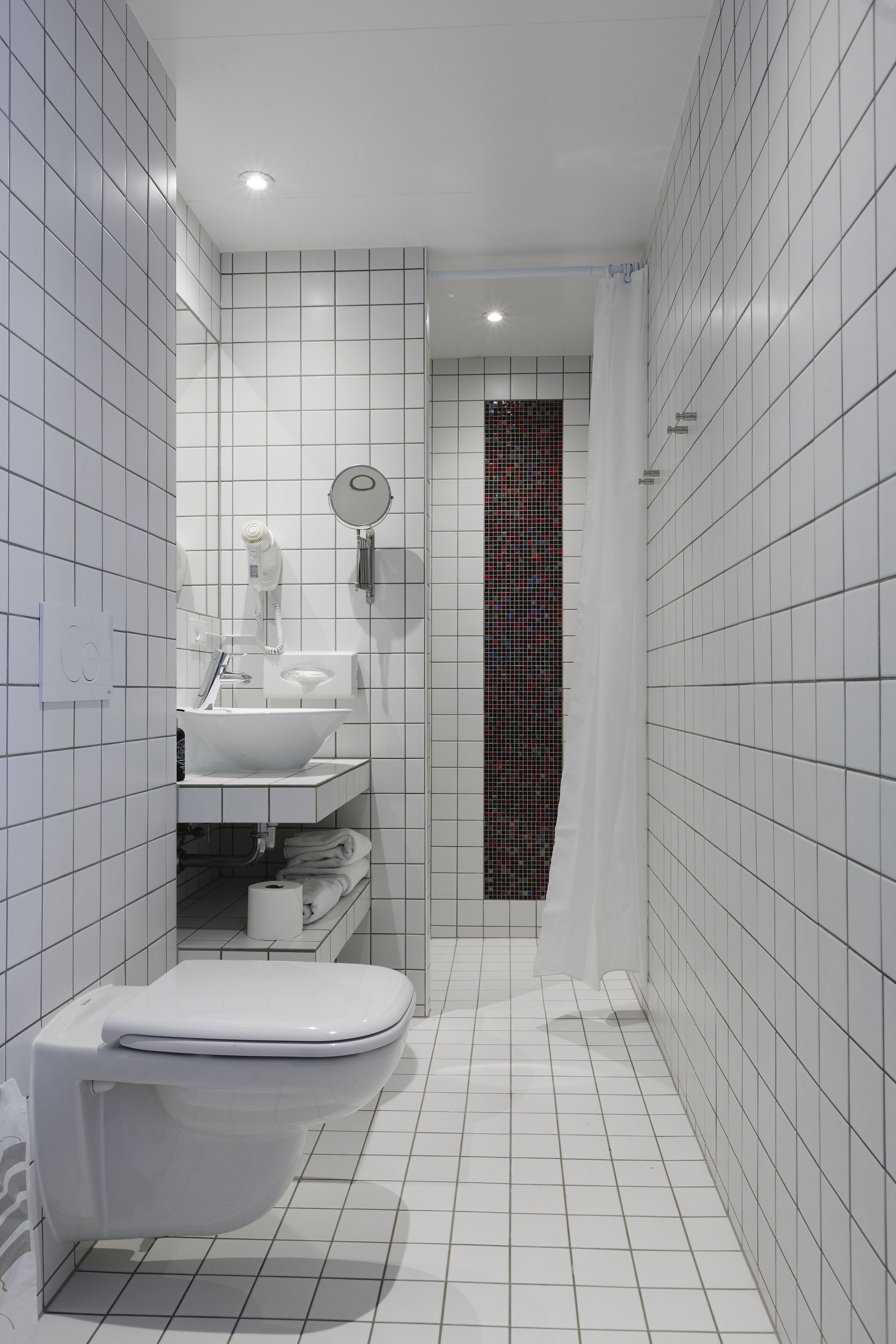 Een moderne badkamer met witte betegelde wanden, een witte wastafel en een toilet.