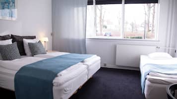 A hotel room with two beds, a window with curtains, a radiator, and a lamp.