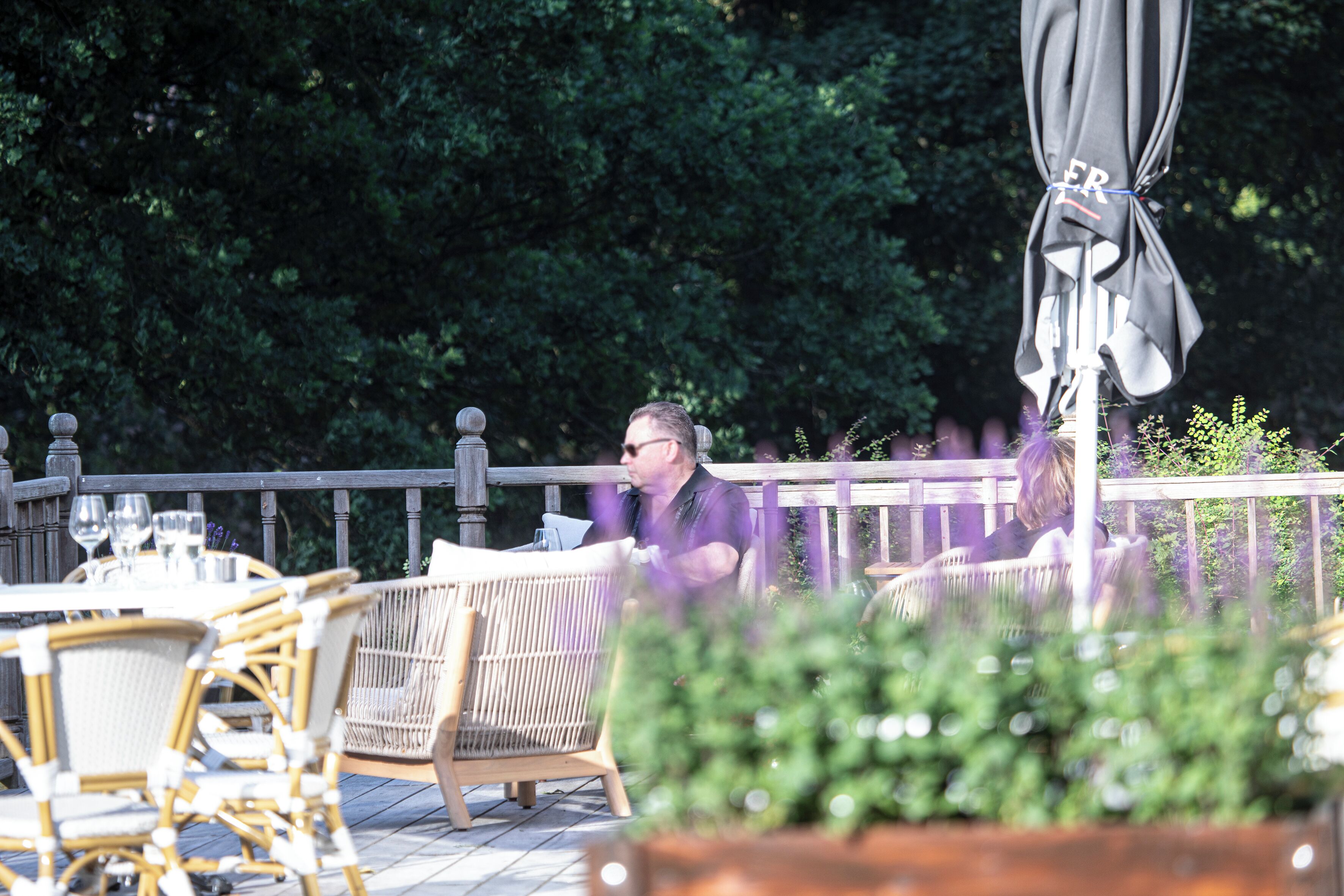 An outdoor patio with wicker furniture, a table set with glasses, and a wooden deck railing.