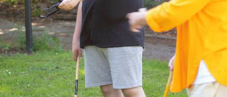 Two people playing croquet in a grassy outdoor area with trees and a fence in the background.