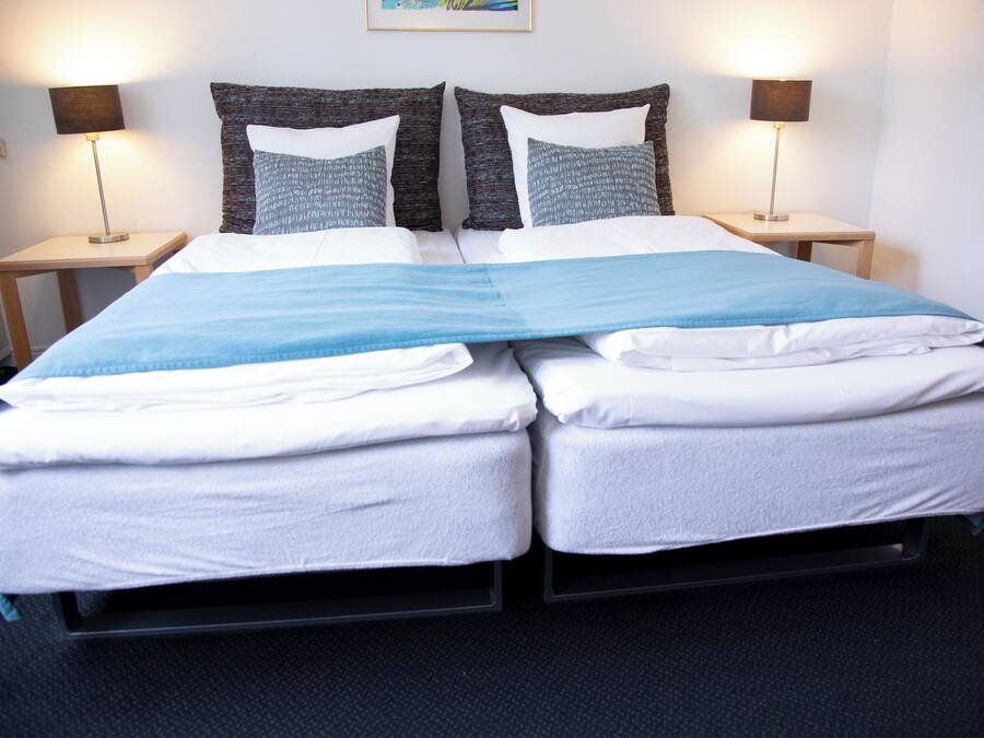 Una cama doble con dos almohadas, un edredón azul y dos lámparas de noche.