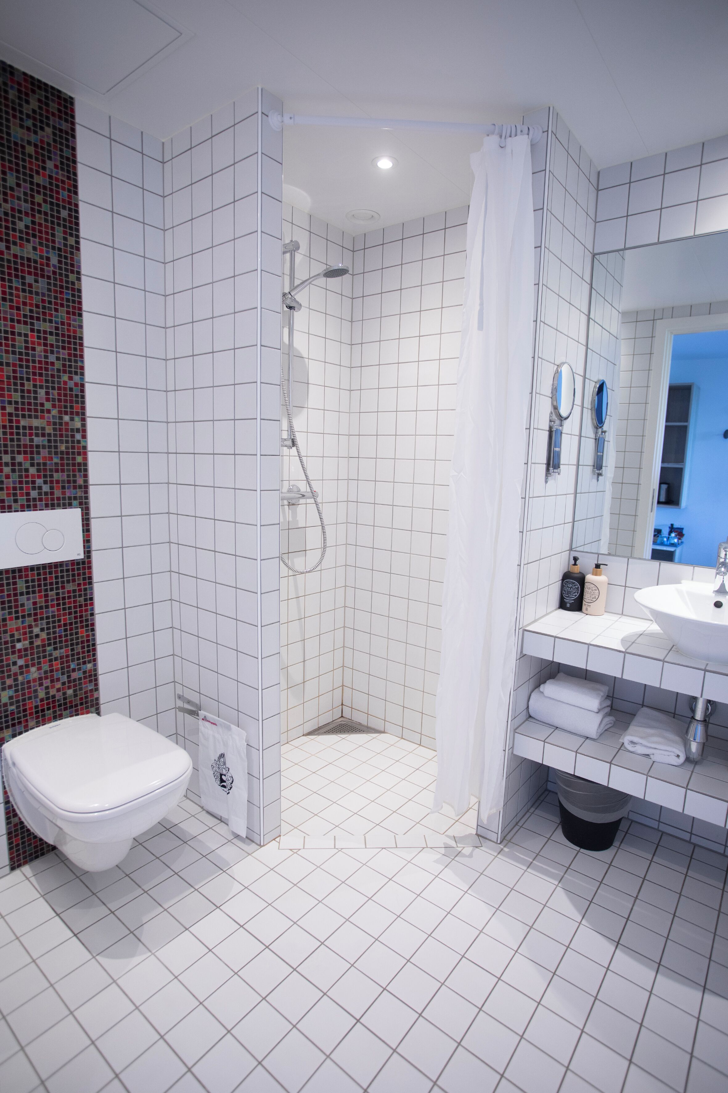 Une salle de bain moderne avec des toilettes blanches, une douche dotée d’une porte en verre et un lavabo avec un miroir.