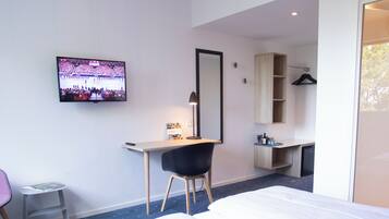 A modern hotel room with a large bed, a desk, a chair, a television, and a wardrobe.