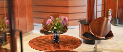 Un área de recepción con un mostrador de madera, una mesa redonda de madera con un jarrón de flores y sillas modernas.