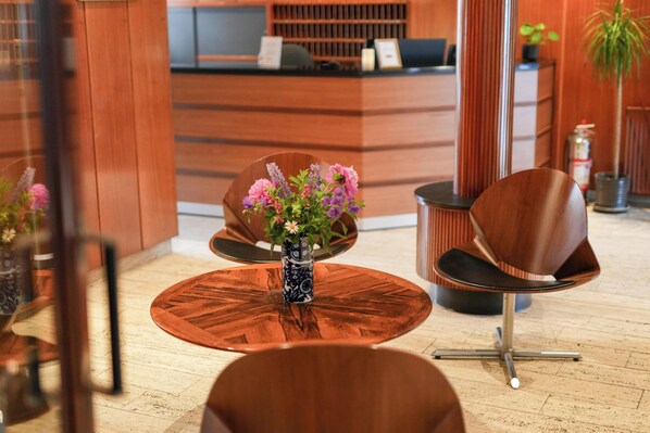 A reception area with a wooden reception desk, a round wooden table with a vase of flowers, and modern chairs.