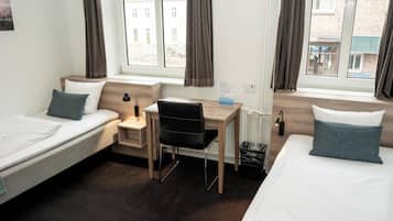 A hotel room with two single beds, a desk, a chair, and a small trash bin.