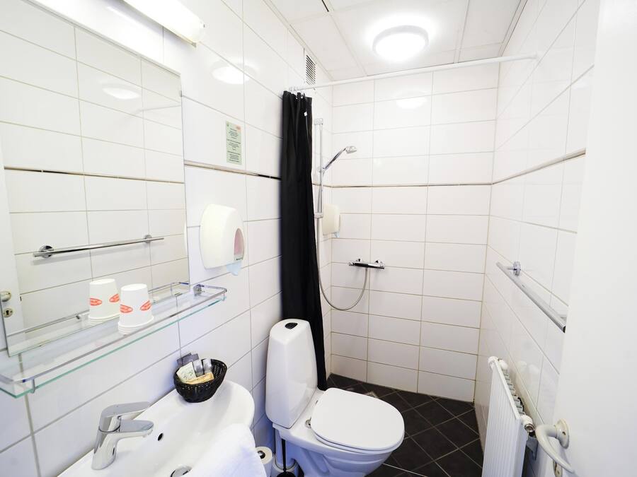 Un baño moderno con lavamanos, inodoro y ducha de color blanco. Incluye un estante de vidrio con artículos de aseo y un espejo sobre el lavamanos.