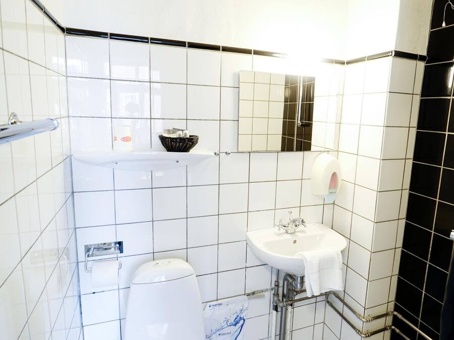 Une petite salle de bain carrelée, équipée de toilettes, d’un lavabo et d’un miroir.
