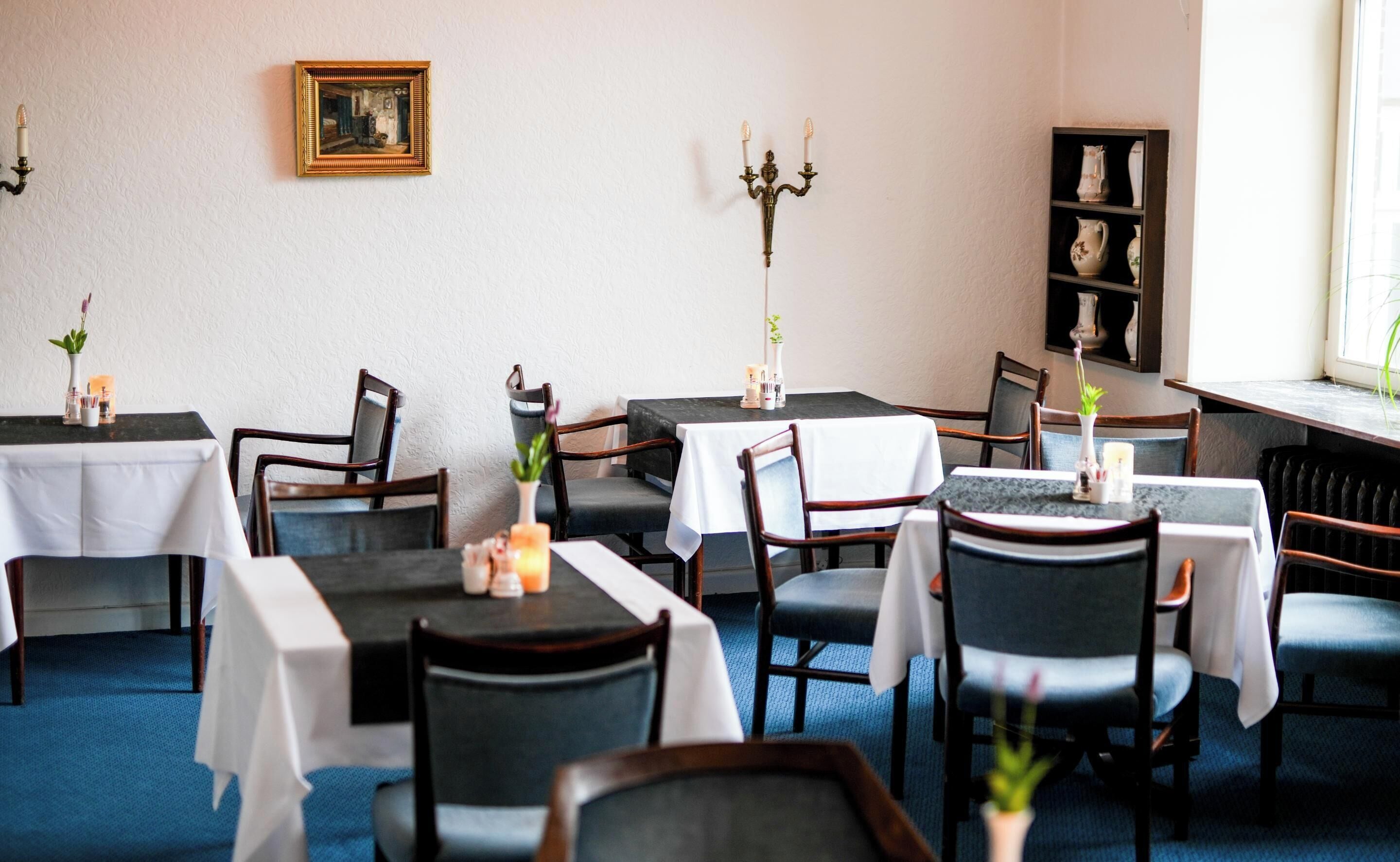A restaurant with multiple tables and chairs, a candelabra, and a shelf with decorative items.