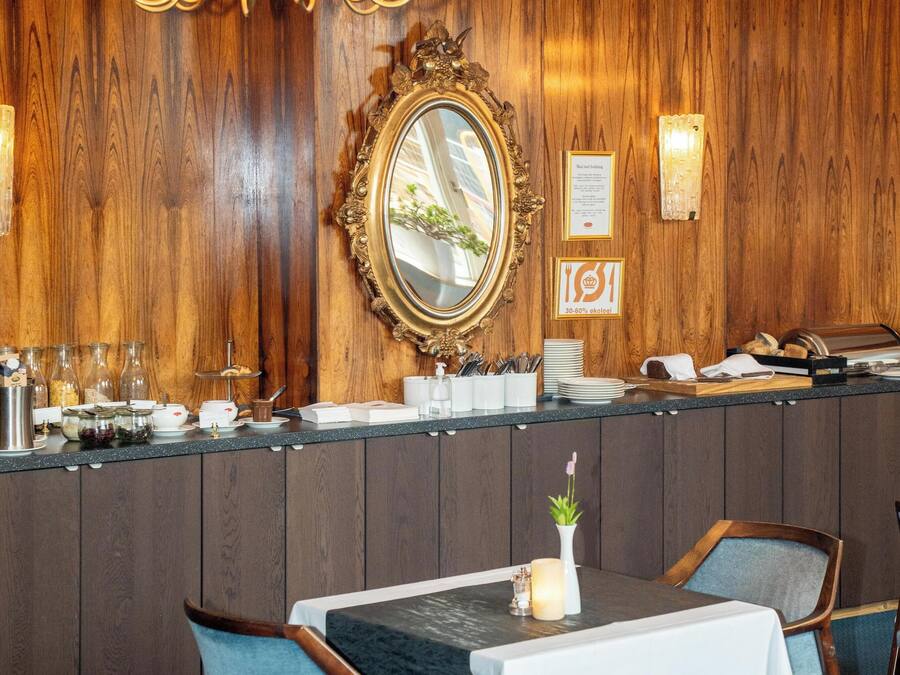 A dining area with a wooden wall, a chandelier, a mirror, and a buffet counter.