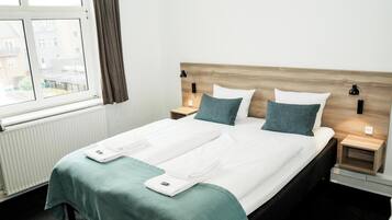 A hotel room with a large bed, two bedside tables, a window with curtains, and a view of buildings outside.