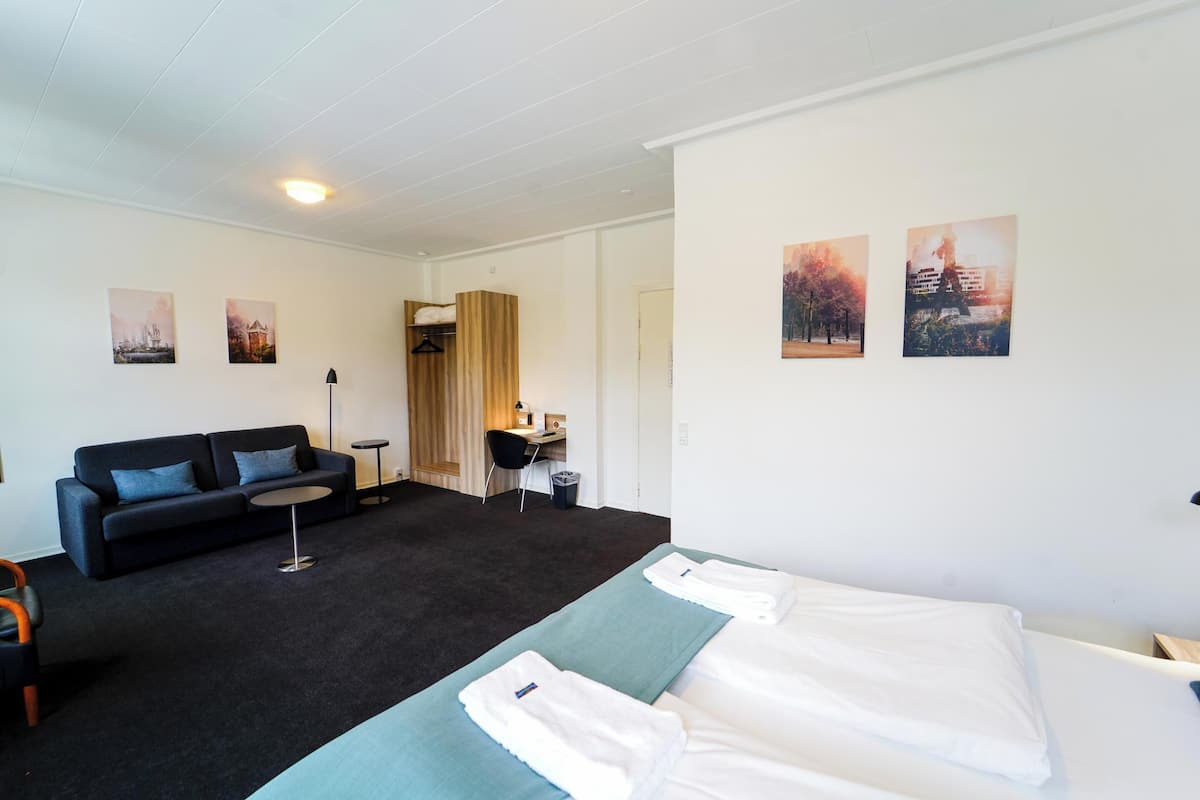 Ein Hotelzimmer mit einer schwarzen Couch, zwei Einzelbetten, einem Schreibtisch und einem Sessel.