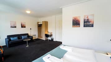 Una habitación de hotel con un sofá negro, dos camas individuales, un escritorio y una silla.