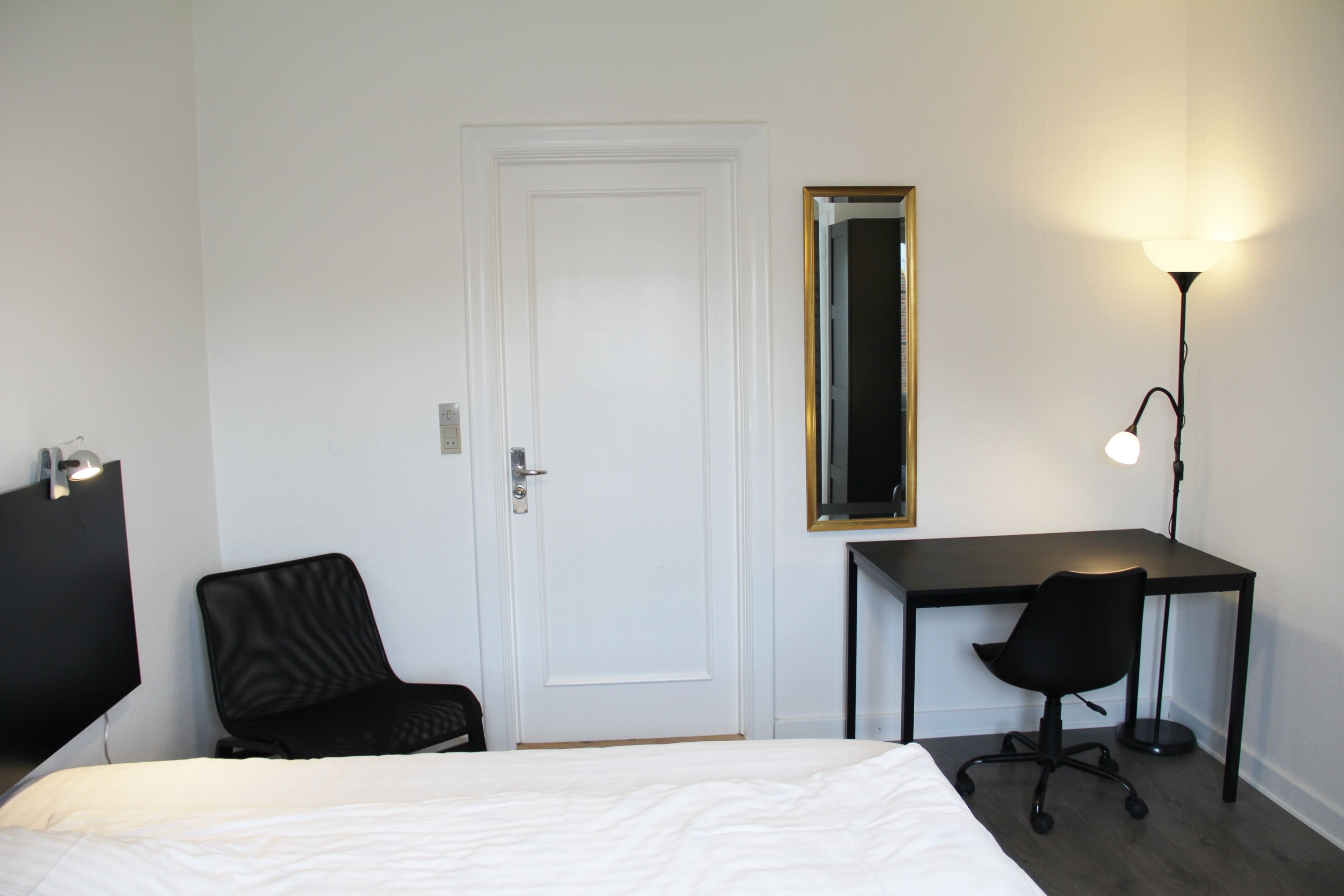 Una habitación de hotel con una cama, un escritorio, una silla, una lámpara de escritorio y un espejo.