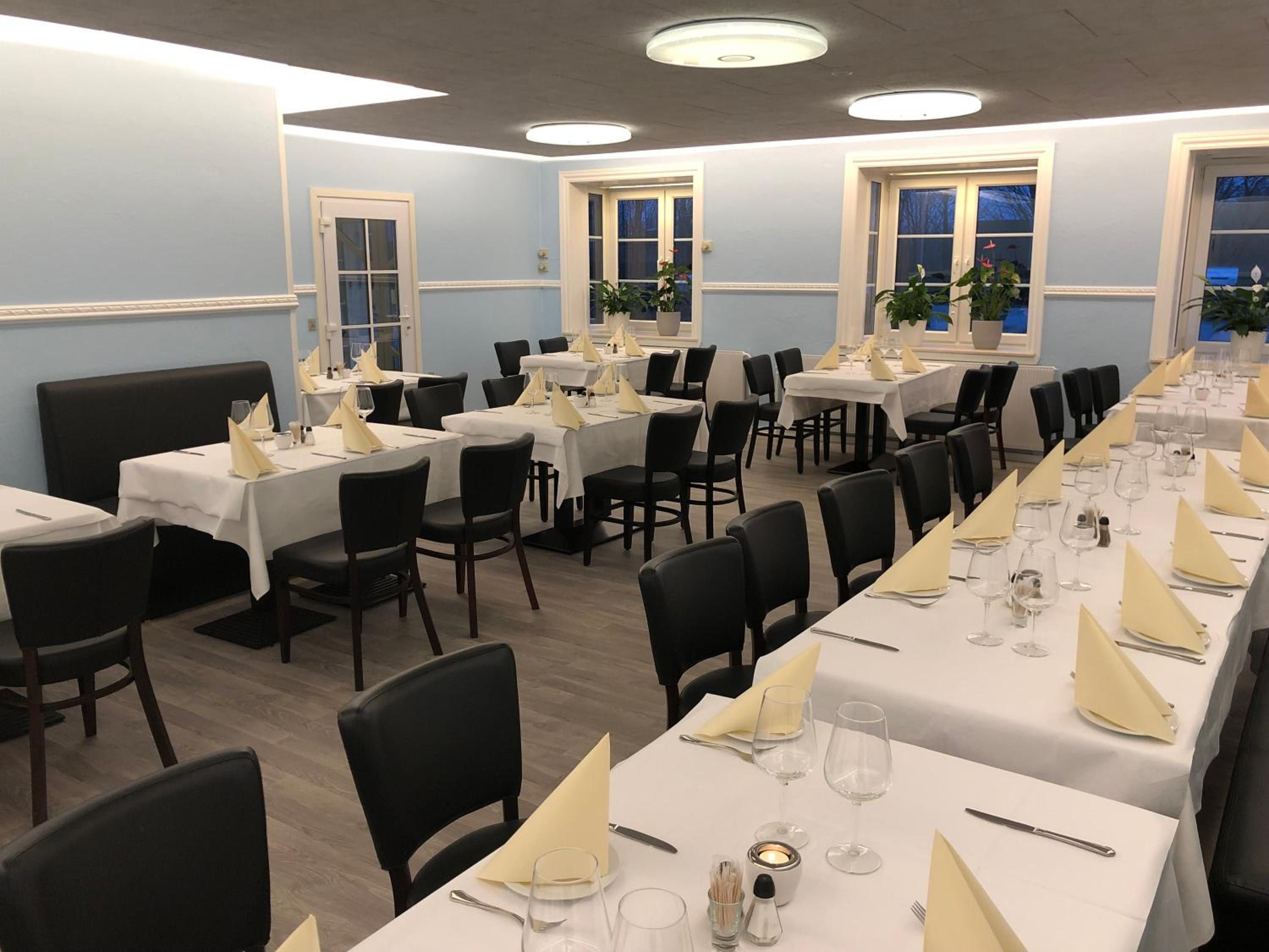 Restaurante com várias mesas preparadas para refeições, com toalhas de mesa brancas, cadeiras pretas e talheres organizados.