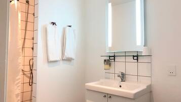 Un baño con ducha, lavamanos y espejo.