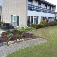 Un edificio moderno con fachada de ladrillo, amplias ventanas y un jardín bien cuidado con diversas plantas y flores.