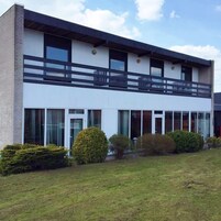 Un edificio moderno de dos pisos con amplios ventanales, techo plano y un balcón en el nivel superior.