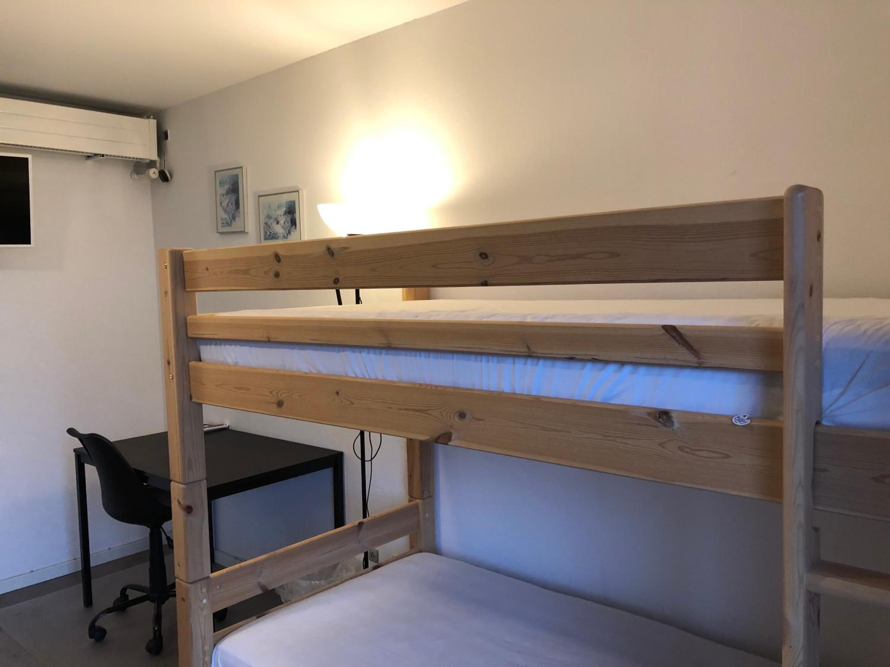 A bunk bed with a desk and chair, a wall-mounted light, and framed pictures.
