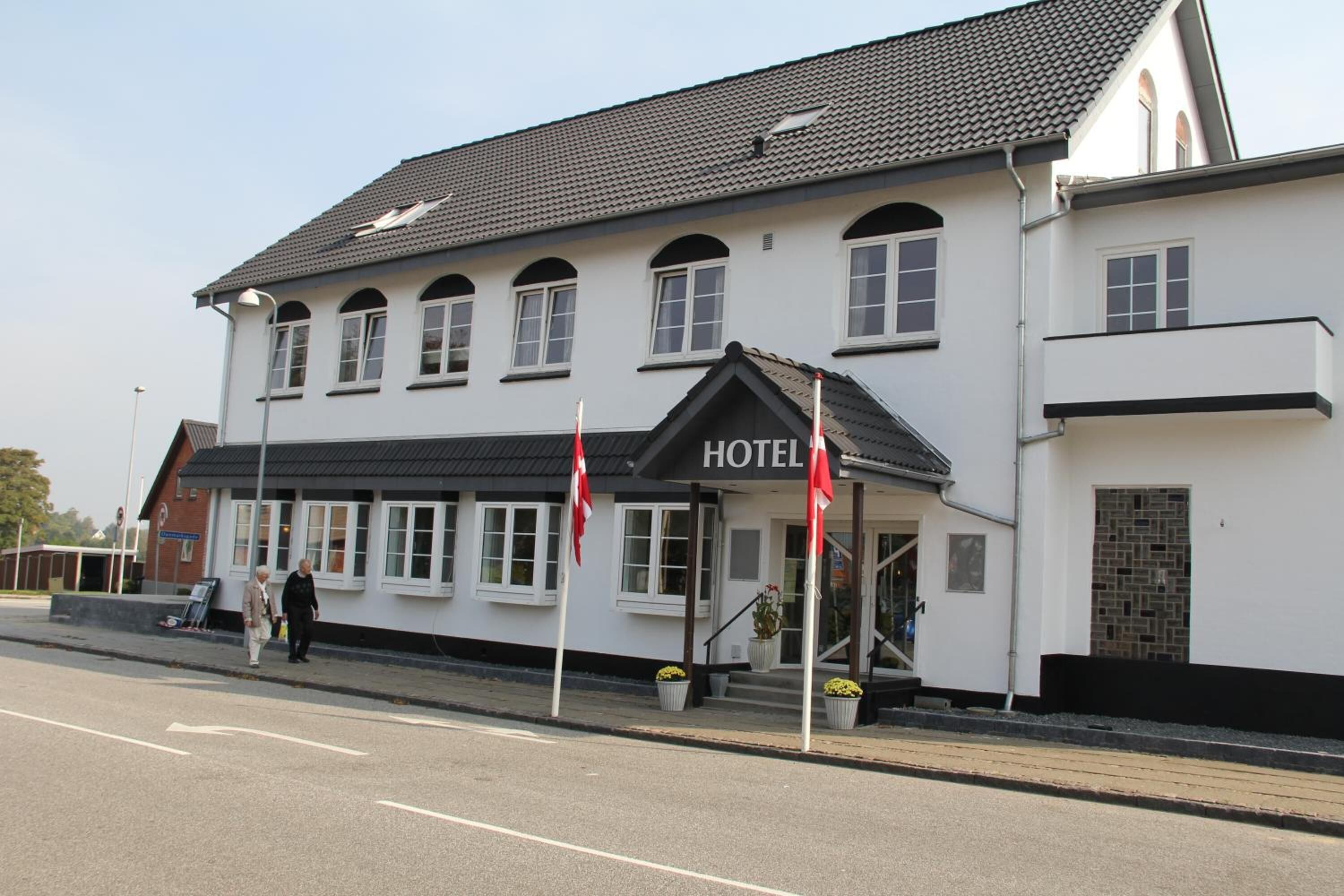 Un hotel de dos pisos con techo negro y paredes blancas, que presenta un llamativo letrero de 'HOTEL' en la entrada.