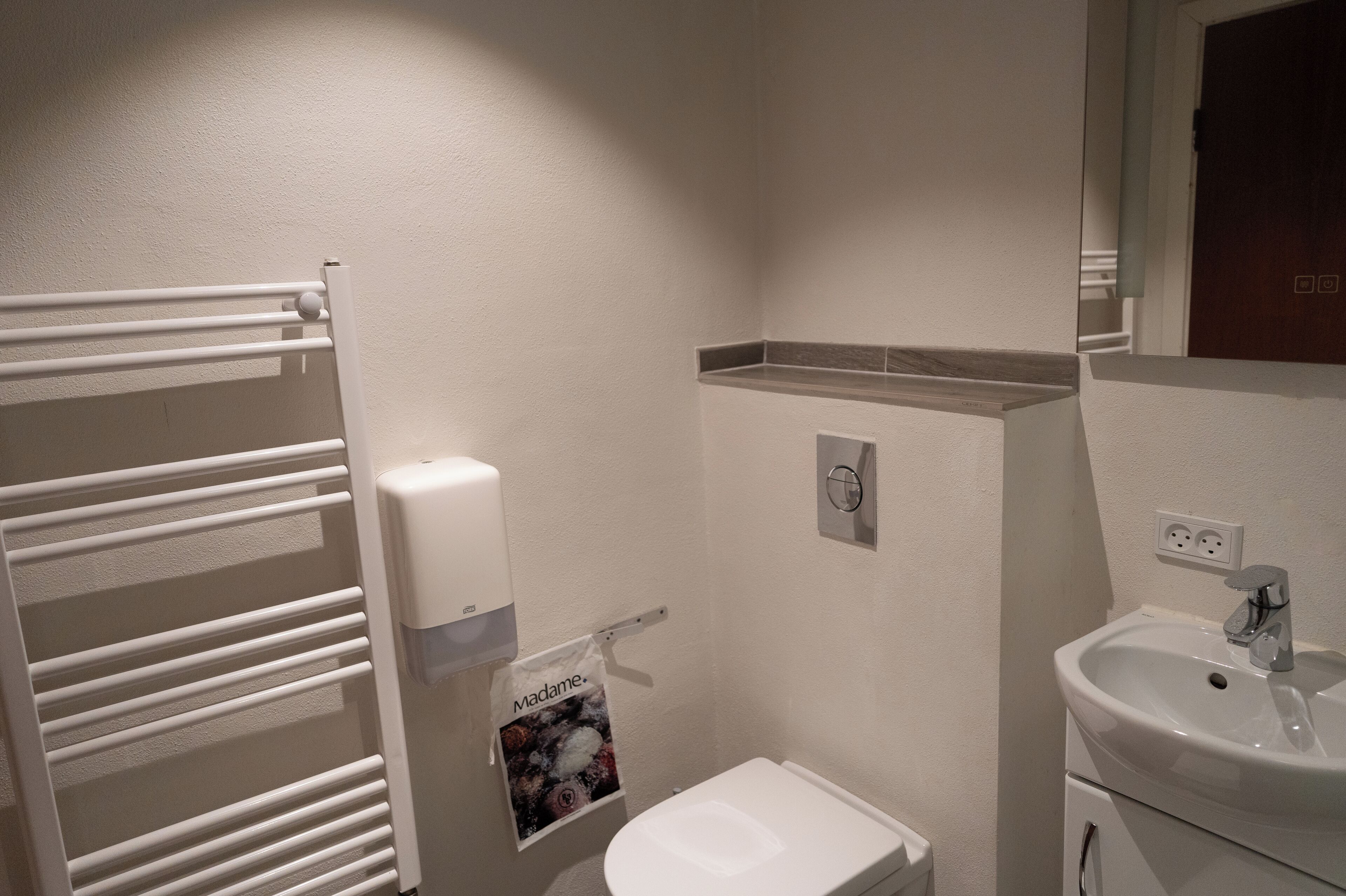 A bathroom with a white toilet, a sink, a towel dispenser, and a towel hanging on a rack.