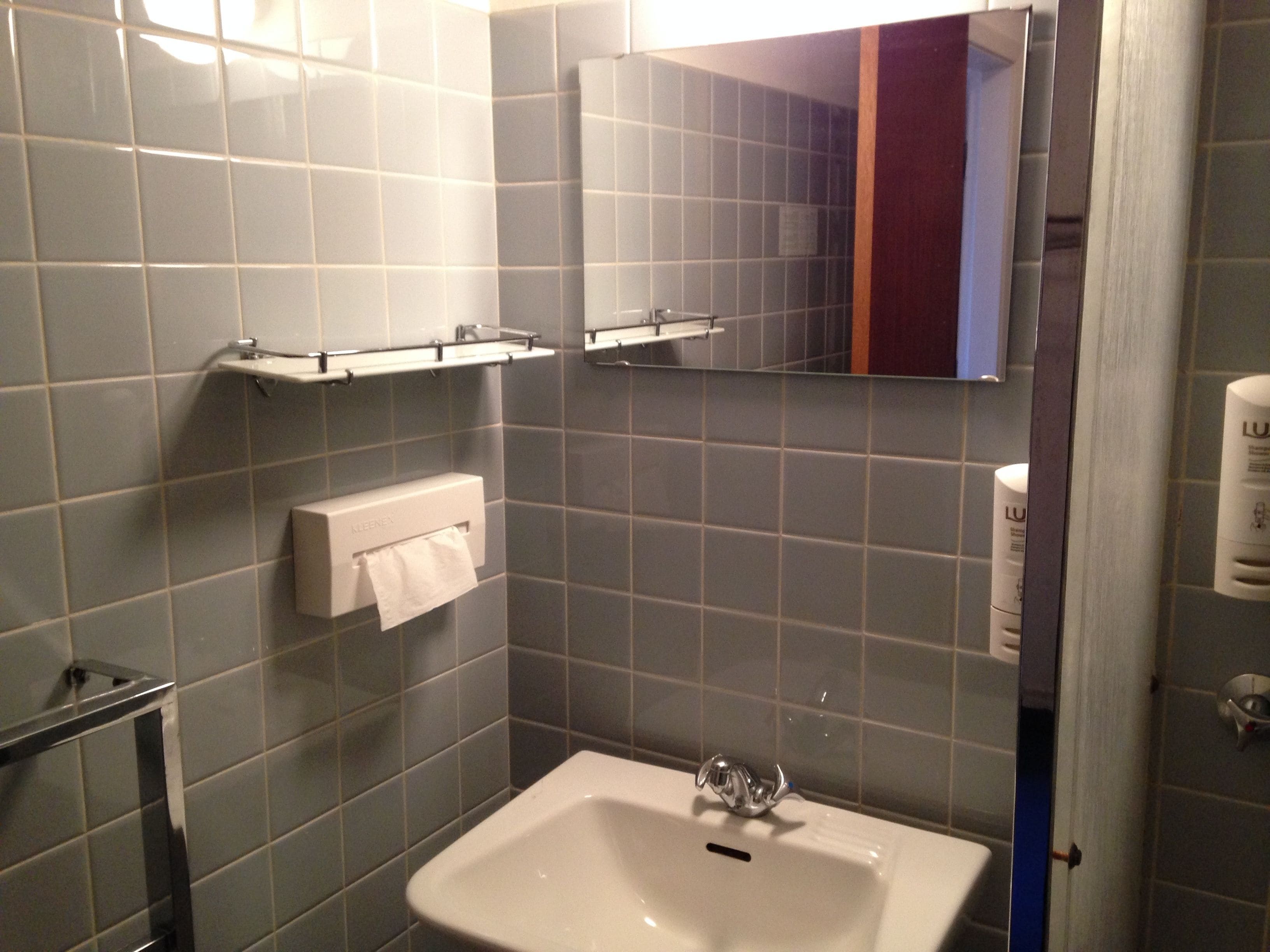 A bathroom with grey tiles, a white sink, and a mirror.