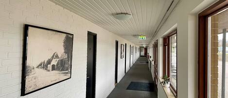 A long hallway with white brick walls, framed black and white photographs, and a door with a keyhole.