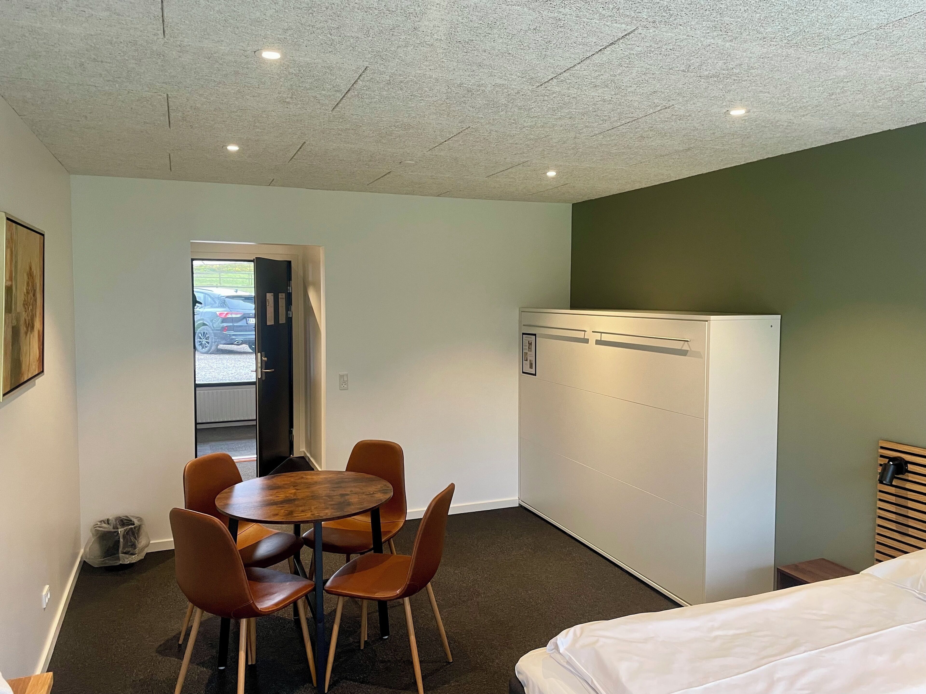 Una camera compatta con un letto, un tavolo da pranzo con sedie, un frigorifero e una porta che dà all'esterno.
