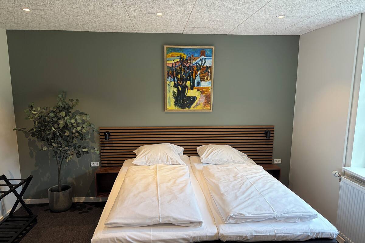 A double bed with white linens, a wooden headboard, and a painting above it.