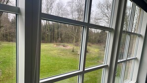 A view through a window with multiple panes, revealing a grassy outdoor area with trees and a clear sky. - Blommenslyst Kro (Blommenslyst)