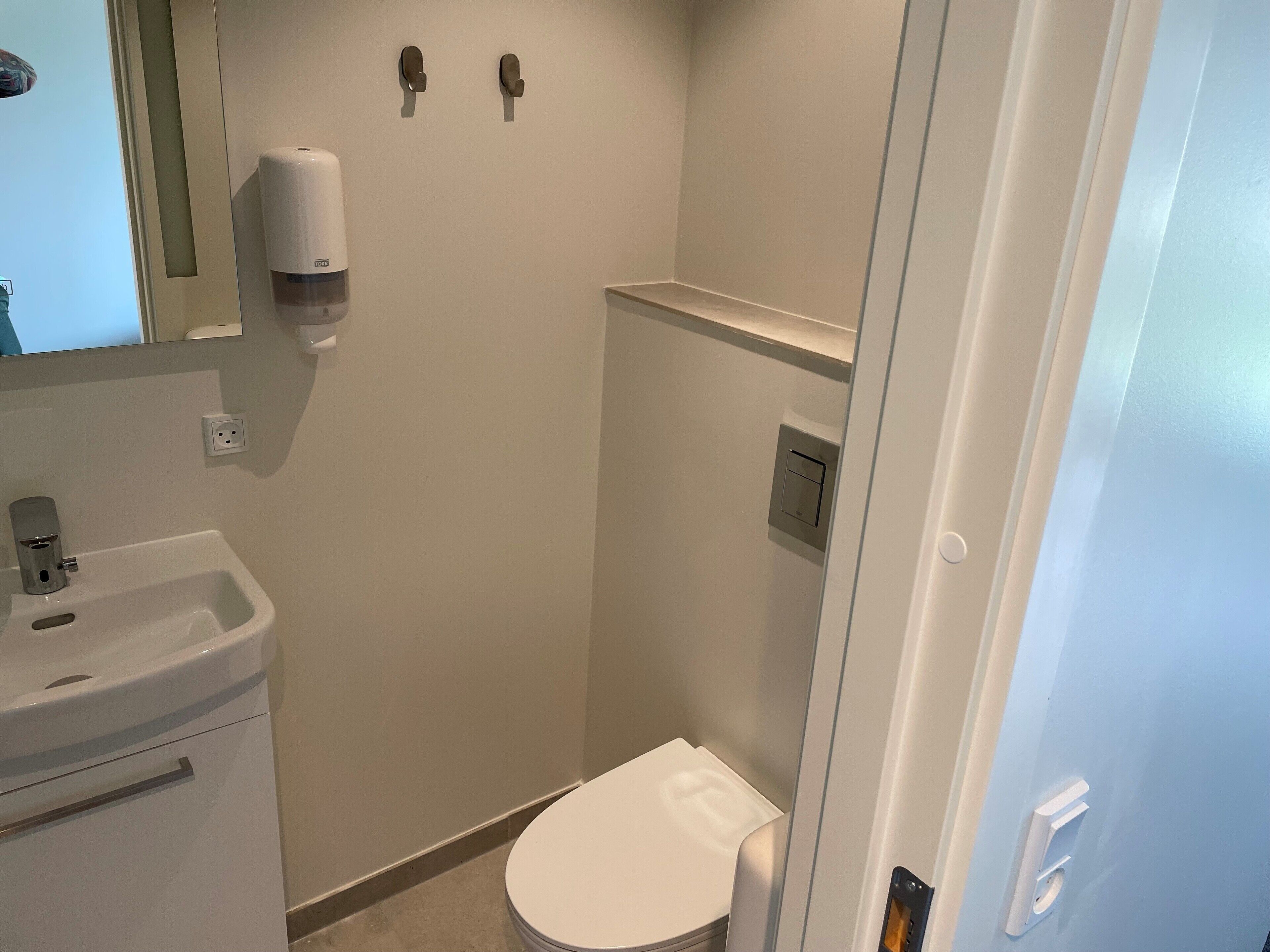 A small, clean bathroom with a toilet, sink, and hand dryer.