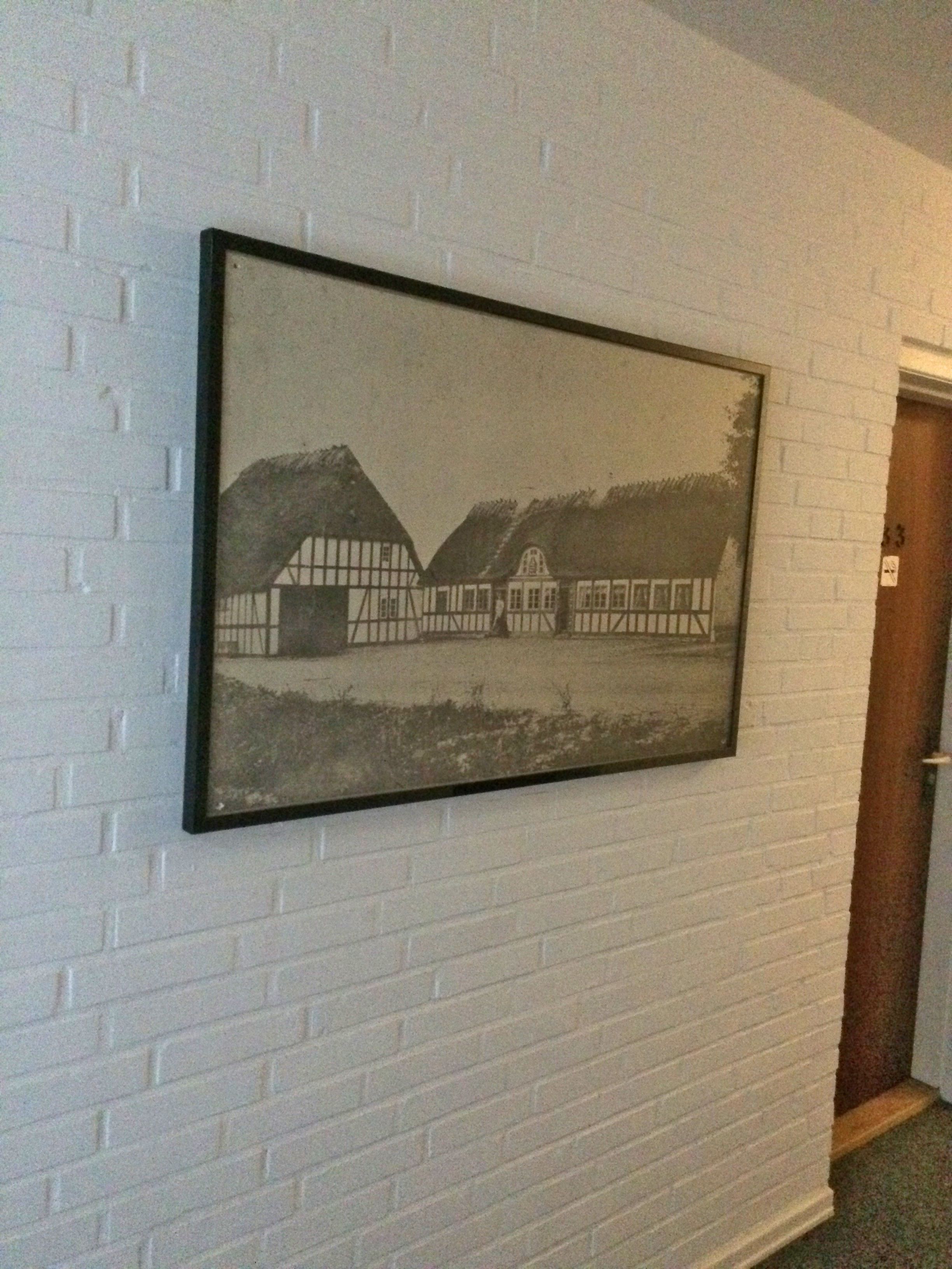 A framed black and white photograph of a traditional half-timbered building on a white brick wall.