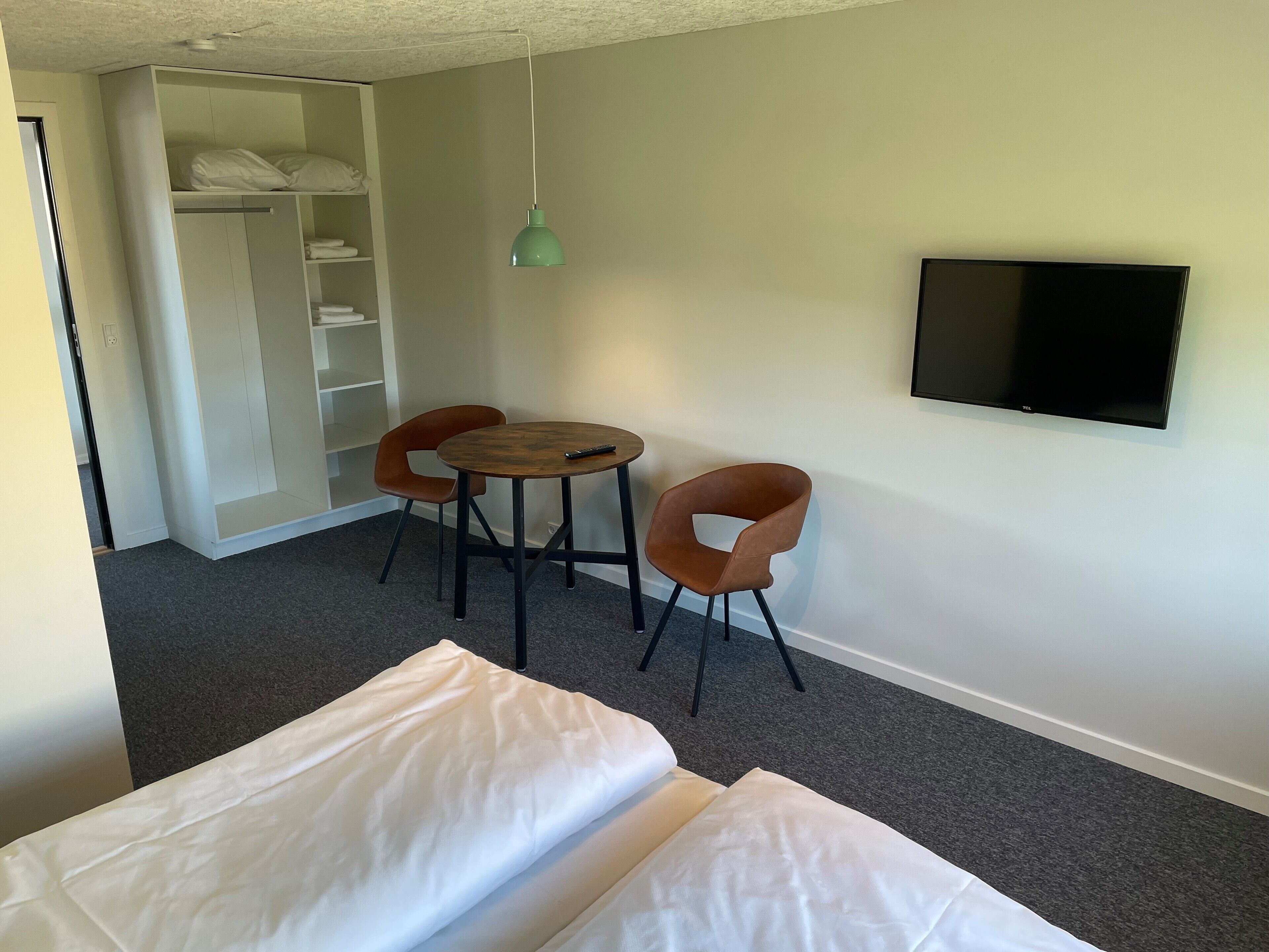 A small room with a bed, two chairs, a table, a TV, and a wardrobe.