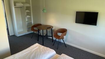 A small room with a bed, two chairs, a table, a TV, and a wardrobe.