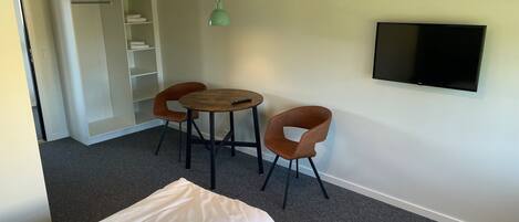 A small room with a bed, two chairs, a table, a TV, and a wardrobe.