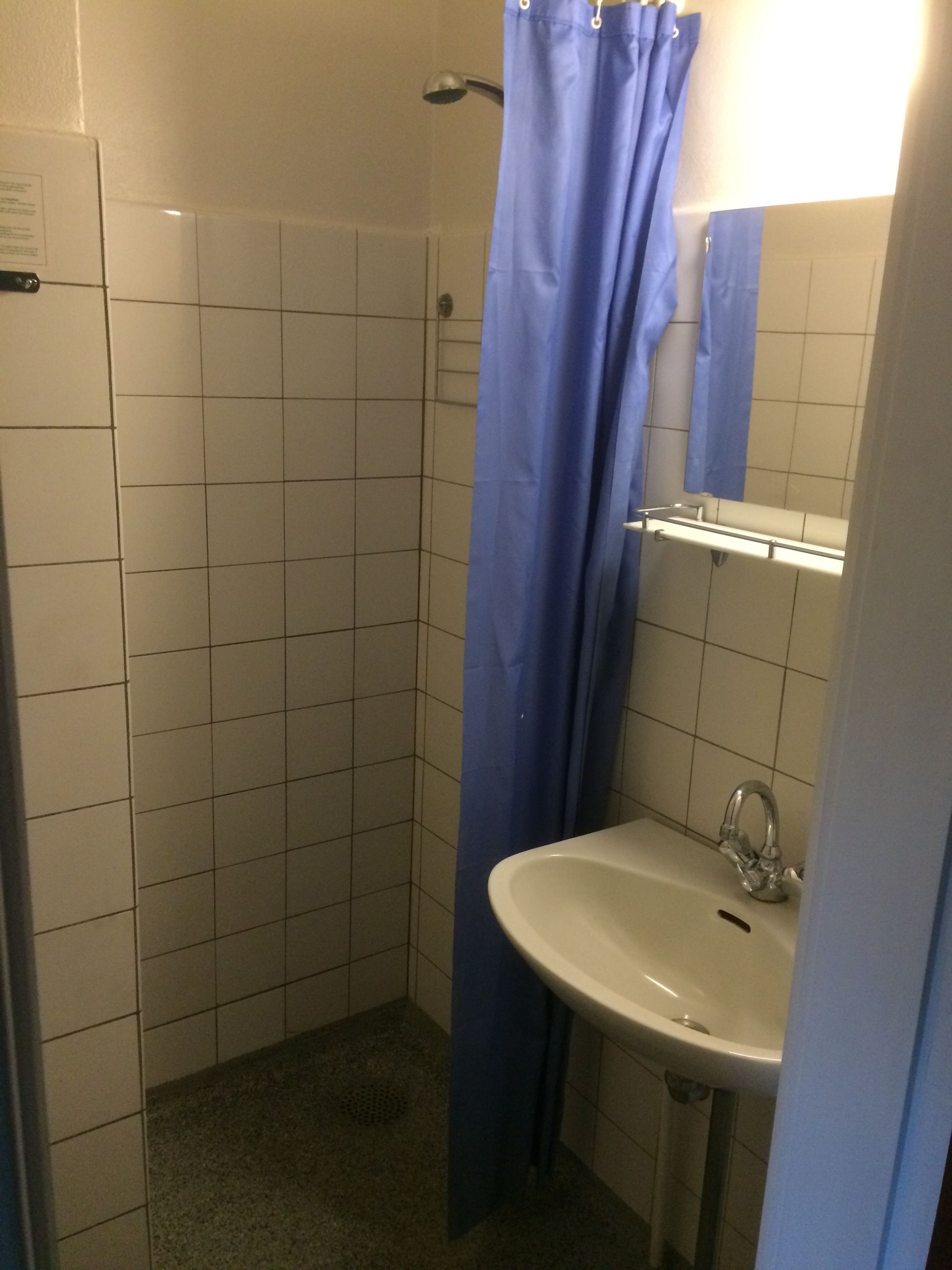 A small bathroom with a shower, a sink, and a mirror.