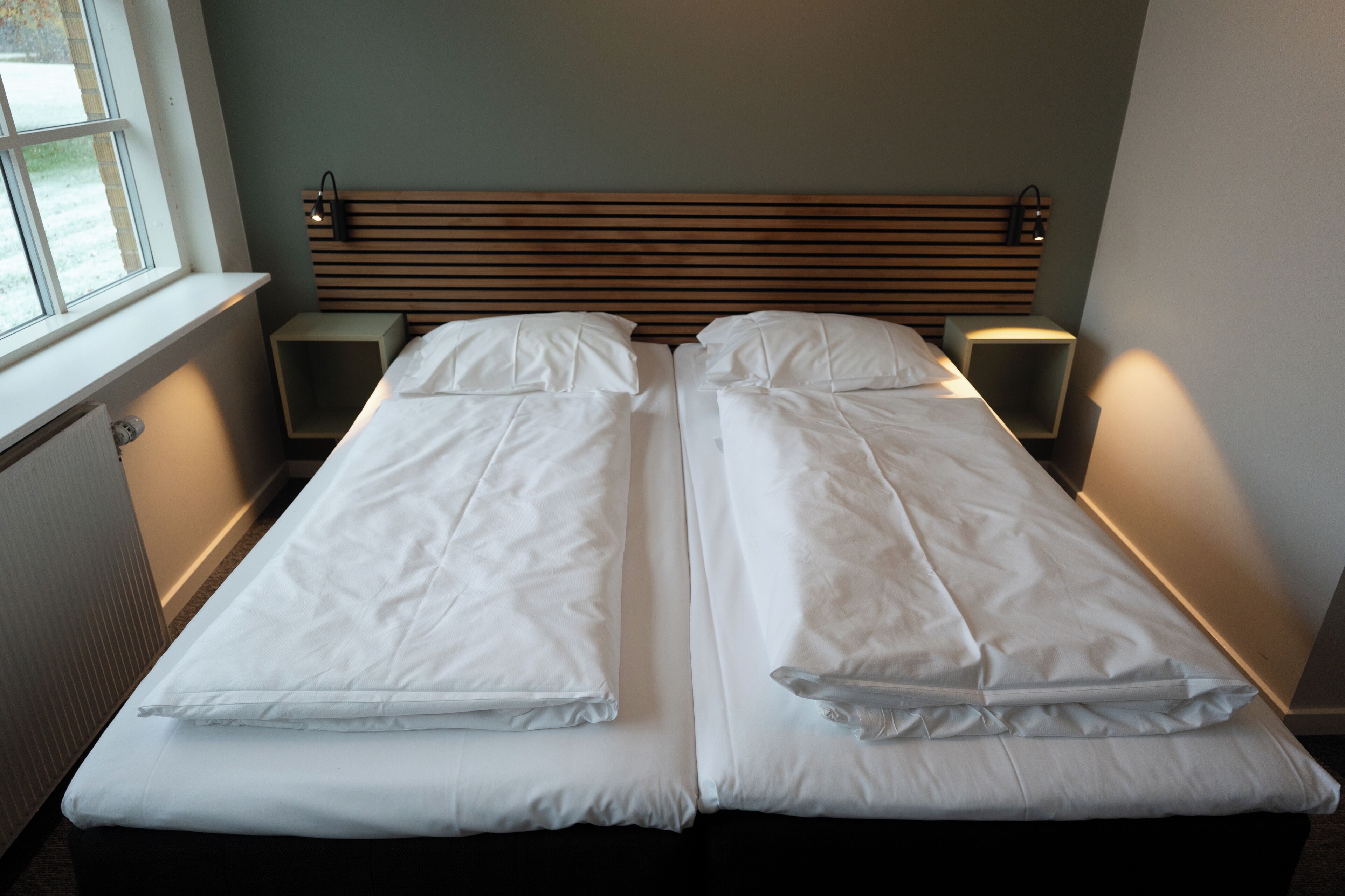 A double bed with white linens, wooden headboard, bedside tables, and wall-mounted lamps.