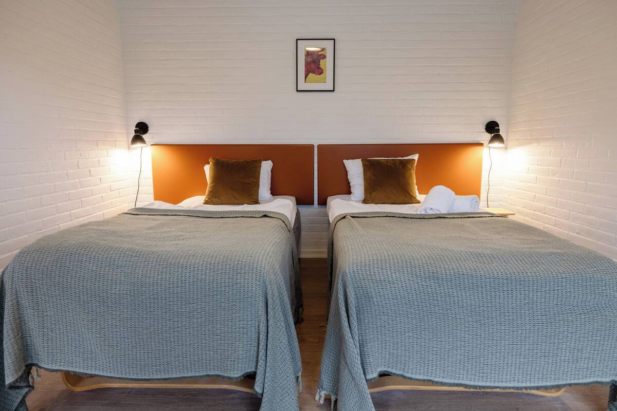 Une chambre avec deux lits, chacun doté d’une tête de lit et d’oreillers, et un tableau encadré accroché au mur.