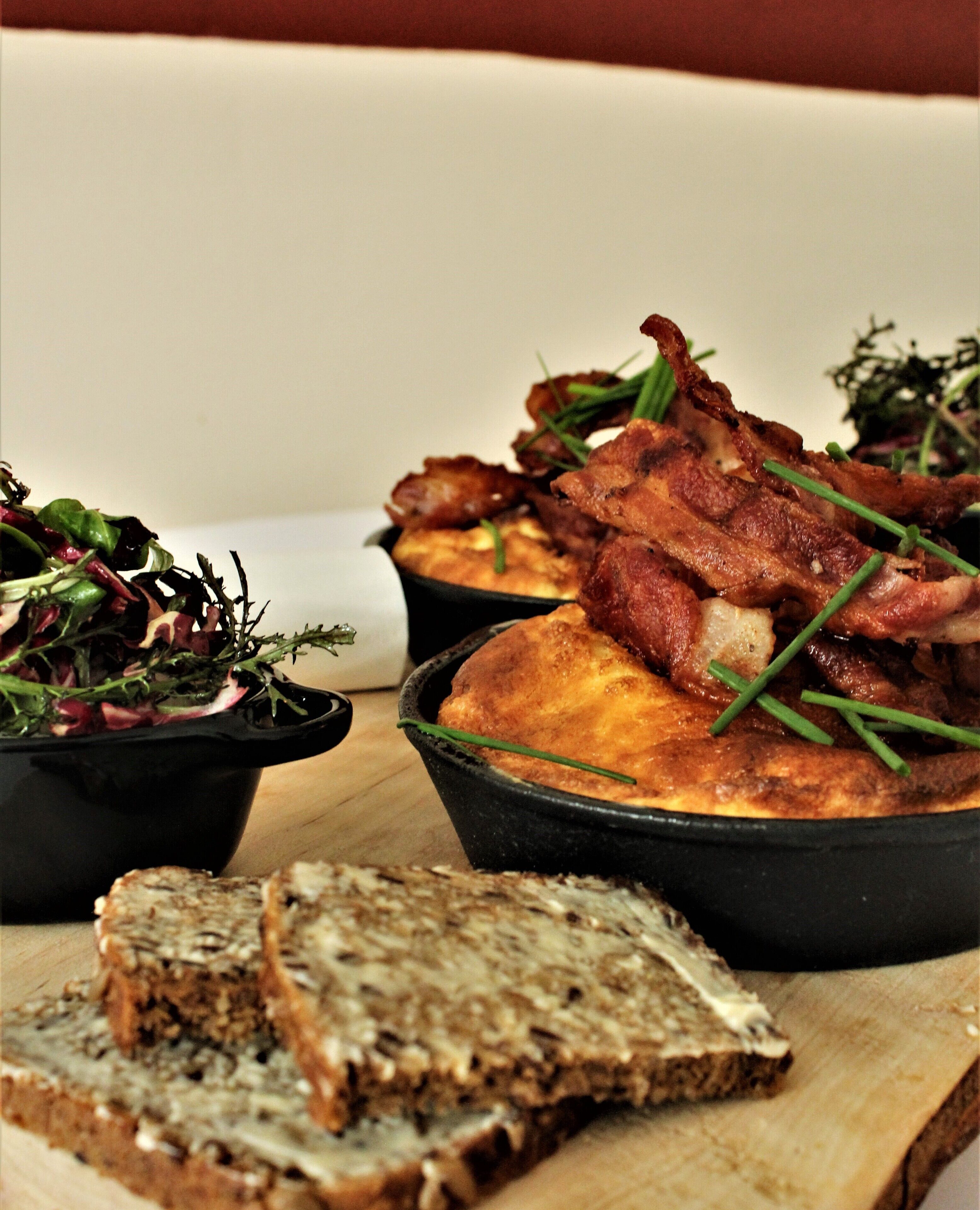 Un plato con tocino, verduras y pan sobre una tabla de madera.