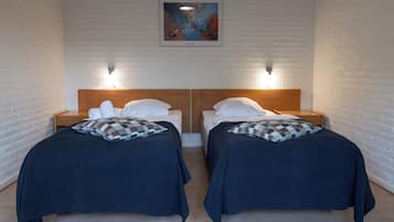 A room with two beds, each with a wooden headboard and white bedding. There is a framed artwork on the wall above the beds.