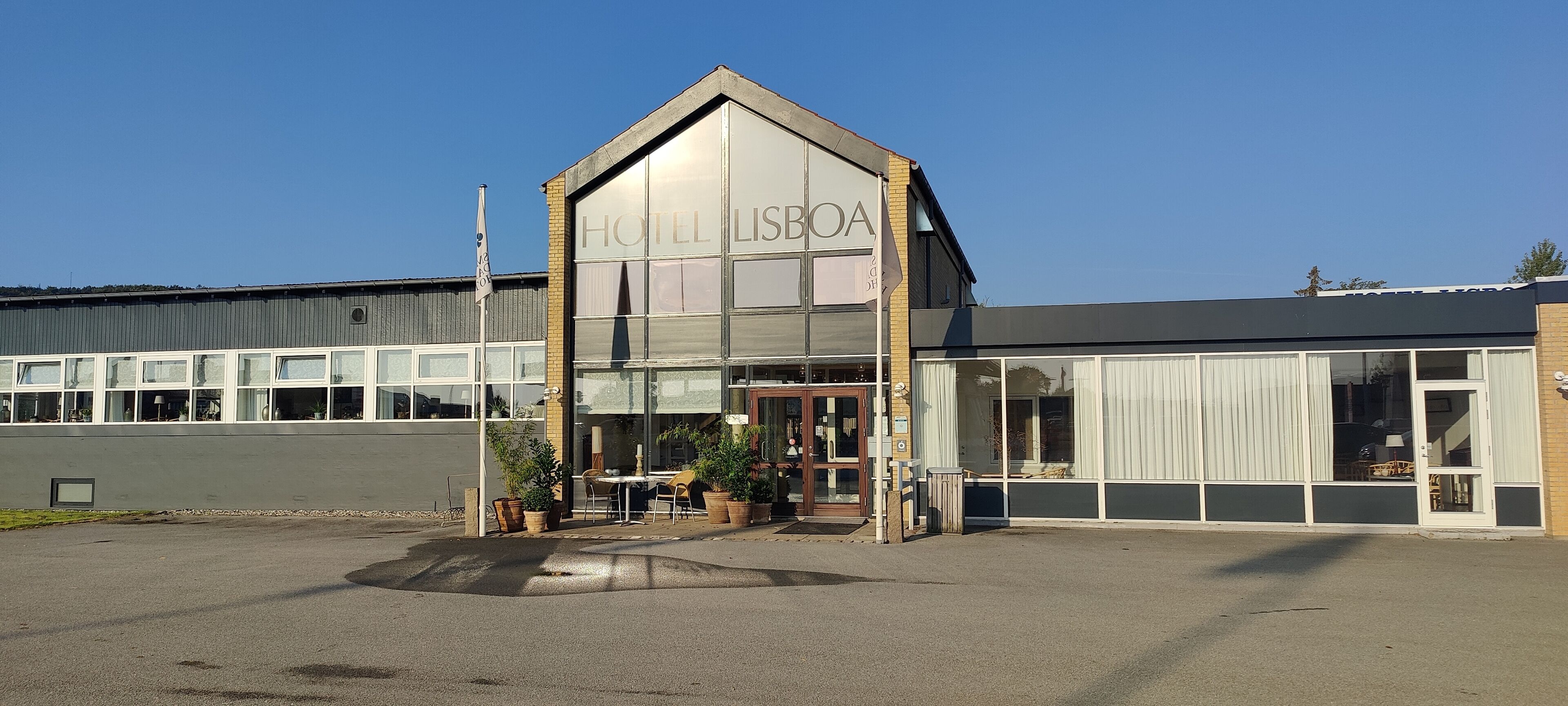 Un edificio moderno con un cartel que dice "HOTEL LISBOA" y un área de estar al aire libre cubierta con mesas y sillas.