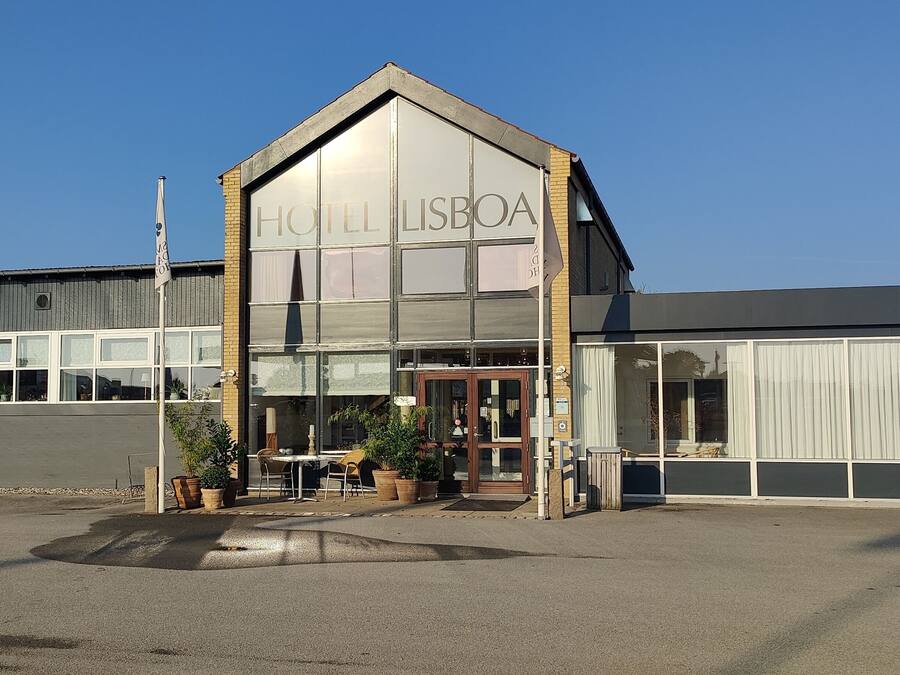 Un edificio moderno con un cartel que dice "HOTEL LISBOA" y un área de estar al aire libre cubierta con mesas y sillas.