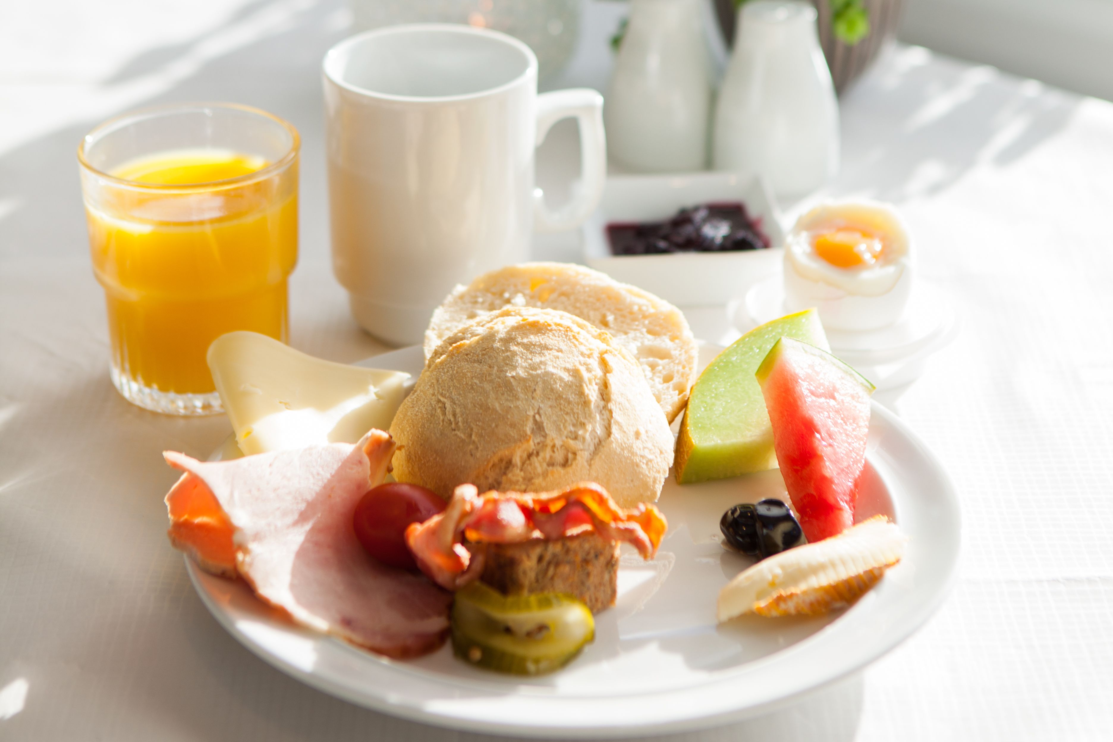 A breakfast plate with ham, bacon, eggs, a biscuit, and fruit.